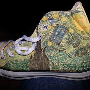May include: A pair of yellow canvas high-top sneakers with a white lace-up closure. The sneakers are painted with a design inspired by Vincent van Gogh's Starry Night, featuring a blue TARDIS from the Doctor Who television series.
