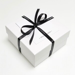 May include: A white gift box with a black ribbon tied in a bow. The ribbon has the text "HOPSCOTCH." printed on it.