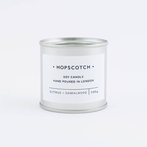 Pode incluir: Uma vela em uma lata de prata com o r&oacute;tulo "HOPSCOTCH" Vela de soja Feita &agrave; m&atilde;o em Londres C&iacute;tricos + S&acirc;ndalo 100g.