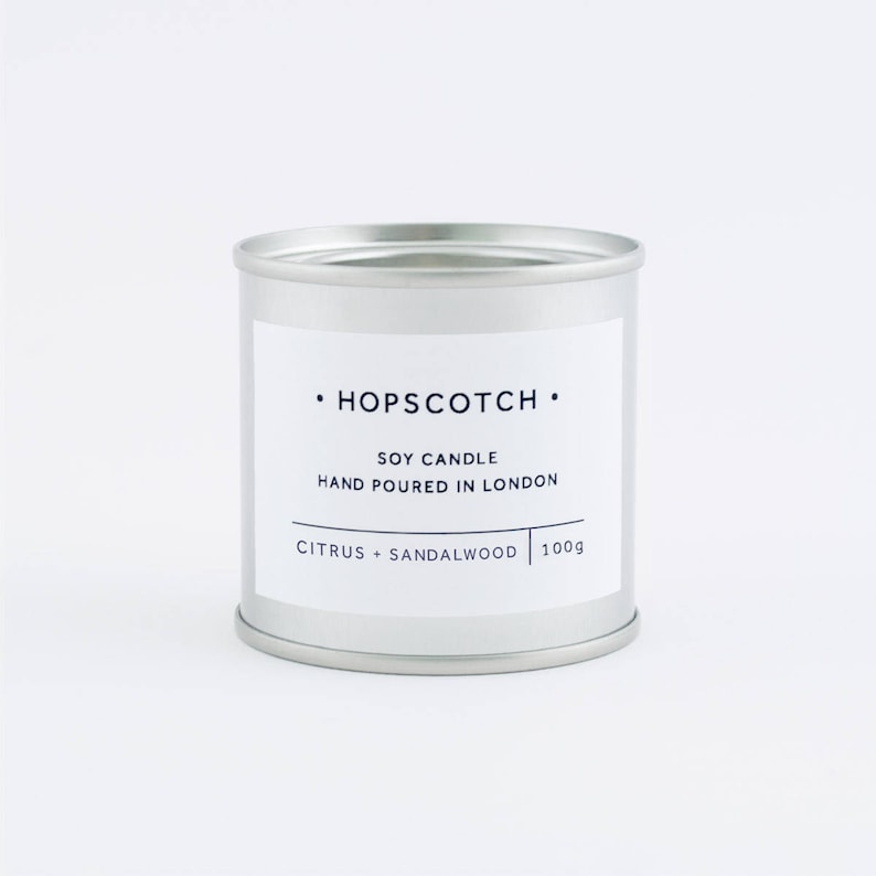 Pode incluir: Uma vela em uma lata de prata com o r&oacute;tulo "HOPSCOTCH" Vela de soja Feita &agrave; m&atilde;o em Londres C&iacute;tricos + S&acirc;ndalo 100g.