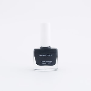 May include: A dark grey nail polish bottle with a white cap. The bottle is labelled "HOPSCOTCH" and "5 FREE FORMULA VEGAN - 10ML".