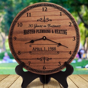 May include: A wooden clock with a black face and hands. The clock is engraved with the text "30 Years in Business Master Plumbing & Heating April 1, 1988".