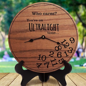 May include: A wooden clock with a black stand. The clock face has the text "Who cares? You're on ULTRALIGHT time..." and numbers 1 through 12 around the edge.