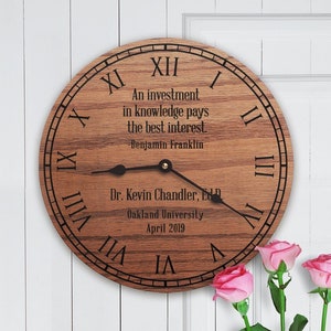Puede incluir: Un reloj de madera con números romanos y una cita de Benjamin Franklin: "Una inversión en conocimiento paga el mejor interés." El reloj también incluye el texto "Dr. Kevin Chandler, EdD Oakland University Abril 2019".