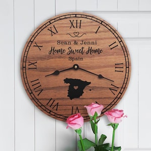May include: A wooden clock with Roman numerals and a map of Spain with a heart in the center. The clock reads "Sean & Jenni Home Sweet Home Spain".