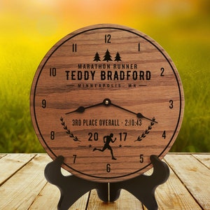 Puede incluir: Un reloj de madera con una esfera negra y agujas negras. El reloj está decorado con una figura corriendo, el texto "Marathon Runner Teddy Bradford - Minneapolis, MN", y el texto "3rd Place Overall - 2:10:43".
