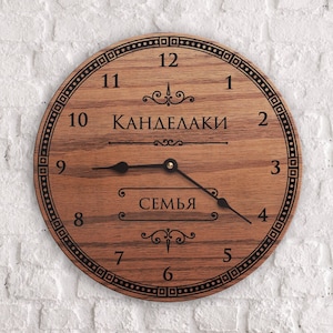 May include: A wooden clock with black hands and Roman numerals. The clock face has the text "Канделаки семья" in black.