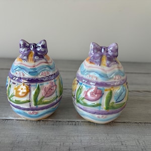 May include: A handmade wooden sign with the text "Welcome" in a playful font. The sign is painted white with a distressed finish, and features a decorative floral design in shades of pink and green. It measures approximately 12 inches wide.