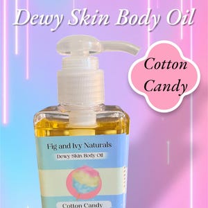 May include: A clear, square bottle of "Cotton Candy" scented "Dewy Skin Body Oil" by Fig and Ivy Naturals. The bottle has a white pump dispenser and a label with a cotton candy graphic. The background is a gradient of pink and purple with white neon lines.