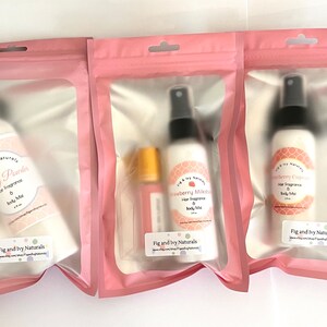 May include: Three pink-packaged body mists and hair fragrances. The bottles are white with black spray nozzles and labels that read "Baby Powder", "Strawberry Milkshake", and "Strawberry Cupcake". Each package has the "Fig and Ivy Naturals" logo.