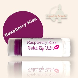 Könnte beinhalten: Eine weiße Tube mit getöntem Lippenbalsam Raspberry Kiss mit einem pinkfarbenen Lippenabdruck auf dem Etikett. Die Tube spiegelt sich in einem Spiegel.