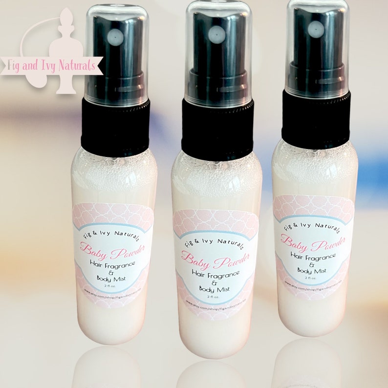 May include: Three clear spray bottles with black caps and pink labels that read "Baby Powder Hair Fragrance & Body Mist". The bottles are filled with a white liquid. The brand name "Fig & Ivy Naturals" is also visible.