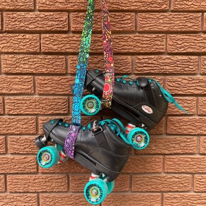 Peut inclure: Paire de patins à roulettes noirs avec des roues et des lacets turquoise, suspendus par une sangle à motifs de points arc-en-ciel. Les patins sont suspendus devant un mur de briques. Les roues ont un design turquoise et argenté.