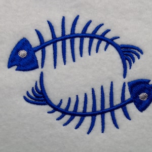 May include: Two blue fish skeletons are intertwined in a circle. The skeletons are embroidered on a white fabric.