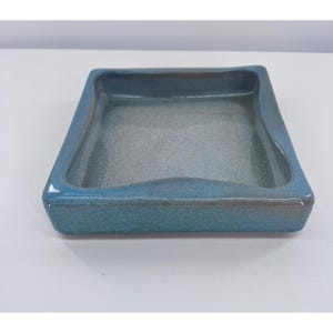 May include: A square, ceramic tray with a slightly curved edge. The tray is a mottled blue-green color with a glossy finish. The interior is a lighter shade of blue-gray. The tray is likely used for serving or display.