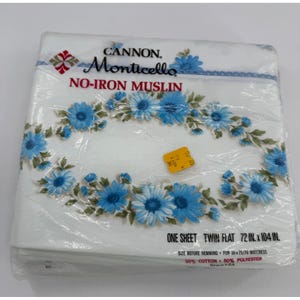 May include: A white Cannon Monticello no-iron muslin twin flat sheet in plastic packaging. The sheet features a blue floral pattern and text stating 183 cm x 264 cm, 50% cotton, 50% polyester, and for 99 cm x 191 cm mattress.