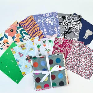 May include: A collection of 12 fabric squares featuring a variety of patterns, including floral, geometric, and polka dots. The squares are tied together with a white ribbon.