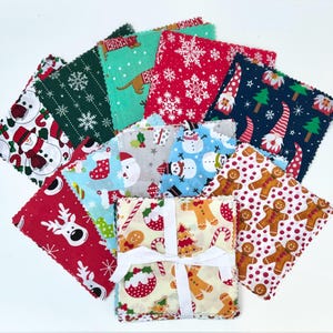 May include: A stack of 10 Christmas-themed fabric squares with various designs, including snowmen, reindeer, gingerbread men, and candy canes. The squares are tied together with a white ribbon.