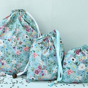 Pode incluir: Três sacos de cordão azul com estampa floral. Os sacos são de tamanhos diferentes e têm cordões brancos.
