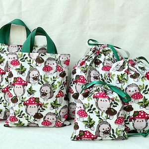 Pode incluir: Conjunto de quatro sacolas de compras reutiliz&aacute;veis com fundo branco e um padr&atilde;o repetido de ouri&ccedil;os e cogumelos. As sacolas s&atilde;o de tecido e t&ecirc;m al&ccedil;as verdes. As sacolas s&atilde;o de tamanhos diferentes.