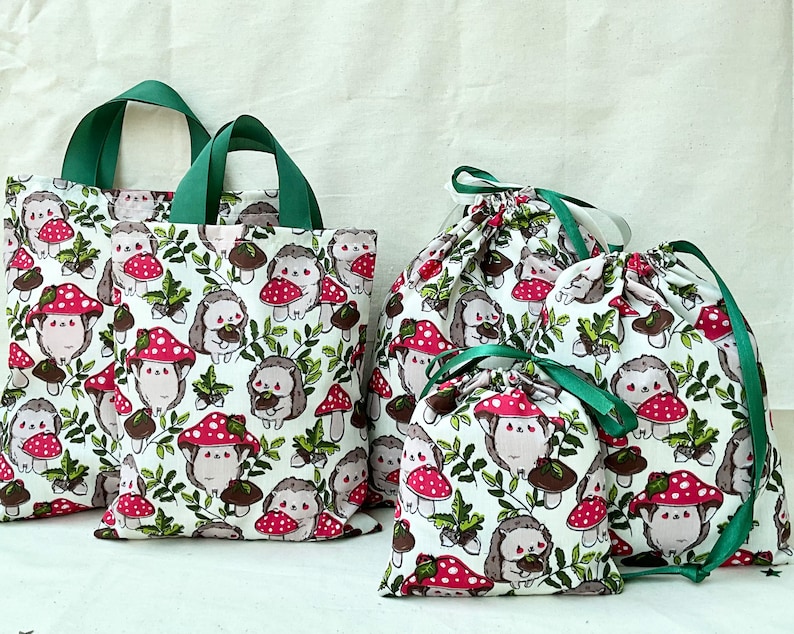 Pode incluir: Conjunto de quatro sacolas de compras reutiliz&aacute;veis com fundo branco e um padr&atilde;o repetido de ouri&ccedil;os e cogumelos. As sacolas s&atilde;o de tecido e t&ecirc;m al&ccedil;as verdes. As sacolas s&atilde;o de tamanhos diferentes.