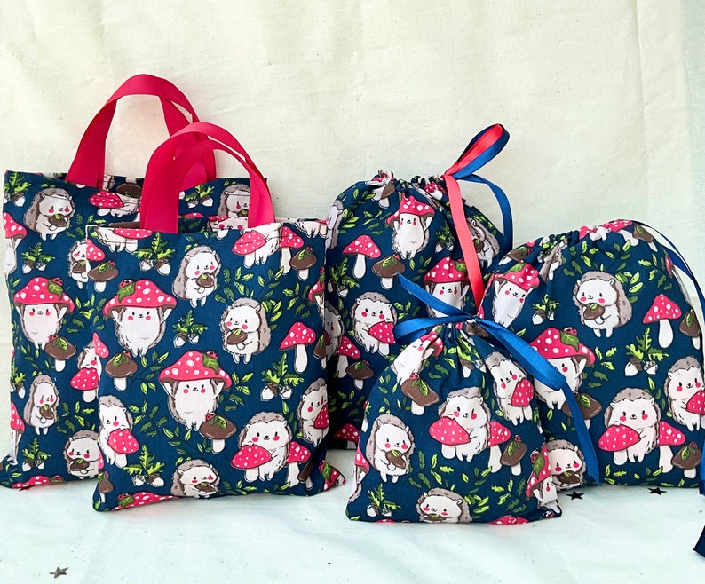 Pode incluir: Conjunto de quatro sacos de tecido azul com estampa de ouri&ccedil;o e cogumelo. Os sacos t&ecirc;m la&ccedil;os de fita vermelhos e azuis.