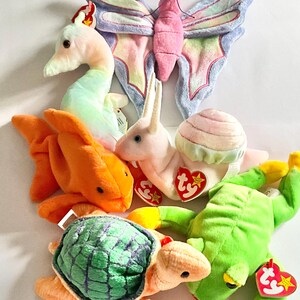 May include: A collection of six plush toys including a pastel butterfly, a light green seahorse, a bright orange fish, a pink snail with a shell, a turtle with a green patterned shell, and a bright green frog, each featuring a red Ty heart tag.
