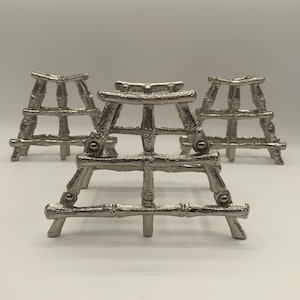 May include: Three silver metal decorative stands in the shape of a ladder. Each stand has a rectangular base and four legs that form a ladder shape. The stands are made of a silver metal that has a brushed finish.