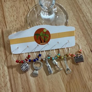 Puede incluir: Juego de seis colgantes para copas de vino con abalorios plateados y cuentas de colores. Los colgantes incluyen una chapa de botella, un abrebotellas, una botella de cerveza, una copa de vino, un abrebotellas y una caja de cerveza. Los colgantes están unidos a una tarjeta blanca y amarilla con un diseño tropical.