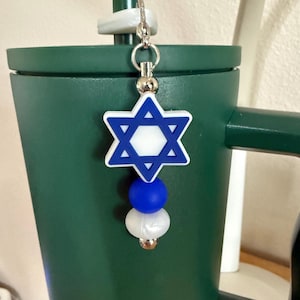 May include: A blue and white Star of David charm with a silver clasp, suspended from a green tumbler. The charm has a blue outline and a white centre, with blue and white beads below.
