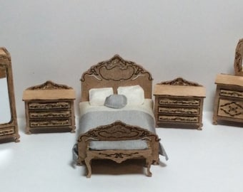 May include: A miniature bedroom set with a bed, two nightstands, a dresser with a mirror, and a wardrobe. The furniture is made of light brown wood with decorative carvings and white accents. The bed has a gray blanket and white pillows.