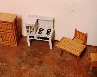 May include: A miniature dollhouse kitchen set with a white cabinet, a black stovetop, a wooden table, and two chairs. The set is made of wood and is painted in a rustic style.