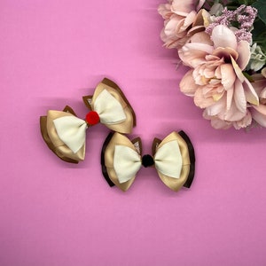 May include: Two brown, beige, and white layered fabric bows with red and black pom-poms in the center.