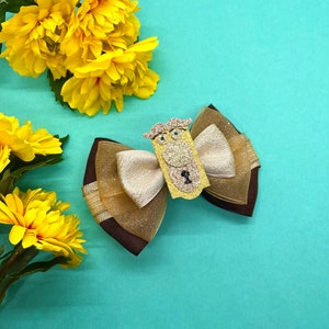 Peut inclure: Un nœud brun et or avec un charme hibou pailleté. Le nœud est fait de tissu transparent et a un ruban de satin brun.