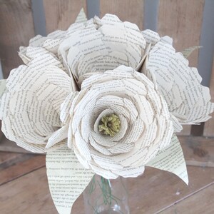 Pode incluir: Um buquê de flores de papel feitas com as páginas de livros antigos. As flores são brancas e têm um centro verde. As flores estão dispostas em um vaso.
