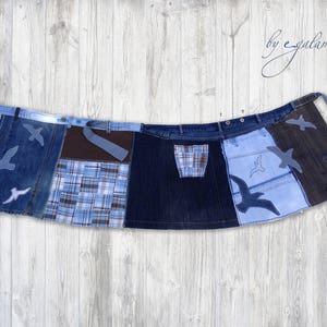 May include: A denim skirt with a patchwork design featuring different shades of blue denim, brown fabric, and plaid fabric. The skirt has a tie closure and features embroidered birds on each panel.
