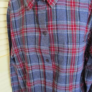 May include: A blue, red, and white plaid flannel shirt with a button-down front and a single chest pocket. The long-sleeved shirt has a classic collar and is made of a soft, woven fabric.