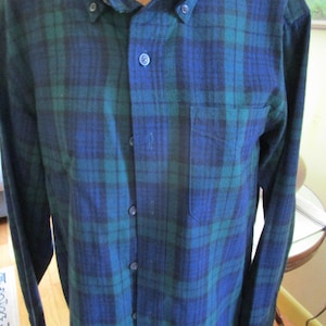May include: A button-down flannel shirt in a classic plaid pattern of blue and green. The long-sleeved shirt has a button-down collar and a single chest pocket. The fabric appears to be a medium weight, suitable for cooler weather.