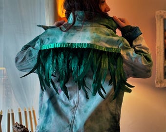 Könnte beinhalten: Eine Jeansjacke mit einem Batik-Muster in Blautönen und Grün. Die Jacke hat eine Reihe grüner Federn, die auf der Rückseite angenäht sind.