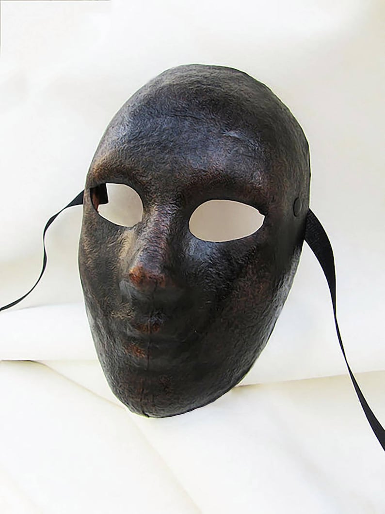 May include: A black masquerade mask with eye holes and a textured surface. The mask has black ribbon ties.