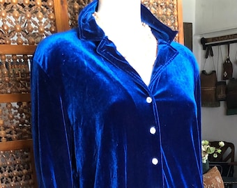 May include: A royal blue velvet two-piece set on a mannequin. The set includes a button-down shirt with a collar and a long skirt. The shirt has long sleeves with blue cuffs. The outfit is displayed in a well-lit room.