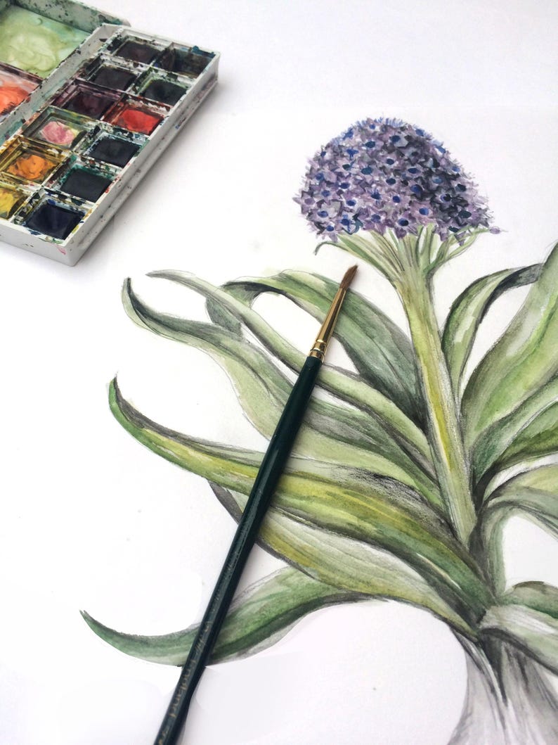 May include: Watercolor painting of a purple flower with green leaves and a paintbrush. A palette of watercolors in various colors is in the upper left corner. The artwork is on white paper.