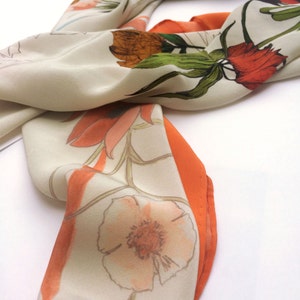 May include: A white silk scarf with a floral print in shades of orange, red, and green. The scarf has a contrasting orange border.