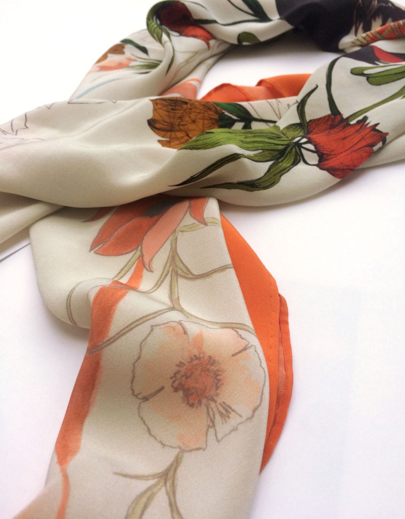 May include: A white silk scarf with a floral print in shades of orange, red, and green. The scarf has a contrasting orange border.