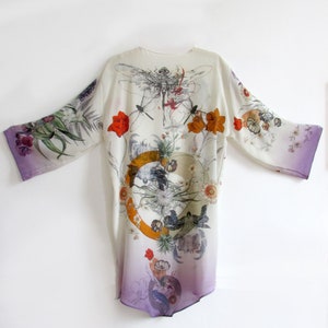 May include: A white kimono-style robe with a floral and dragonfly print. The robe features a gradient from white to purple at the hem and sleeve edges. The design includes orange and red flowers, and a circular graphic.