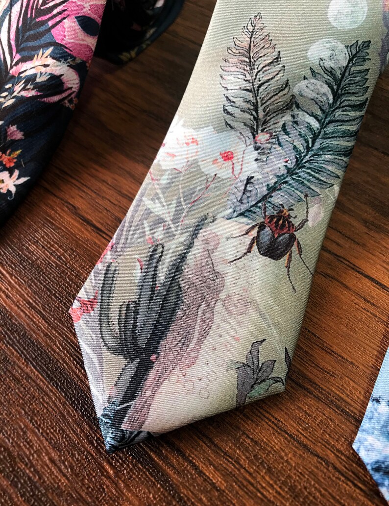 May include: A green silk tie with a floral pattern. The pattern includes pink flowers, green leaves, and a black beetle. The tie is on a wooden surface.