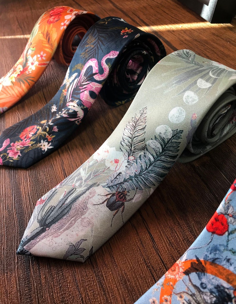 May include: Four patterned neckties, one orange with white flowers, one dark blue with pink flowers and a snake, one light green with a beetle and a fern, and one light blue with red flowers and a bird