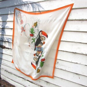 May include: A white silk scarf with an orange border. The scarf features a colorful floral design with two toucans and the text "Fig. 1".