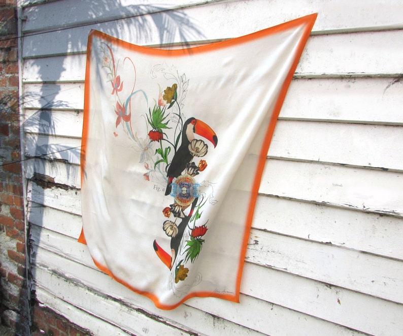 May include: A white silk scarf with an orange border. The scarf features a colorful floral design with two toucans and the text "Fig. 1".