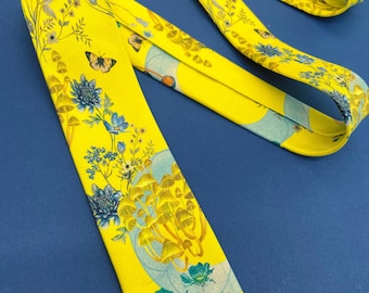 Pode incluir: Uma gravata amarelo-brilhante com uma estampa botânica detalhada de cogumelos amarelos, flores azuis e pequenas borboletas. O tecido tem um acabamento liso com um padrão repetitivo de flora e fungos em tons de azul, amarelo e branco.